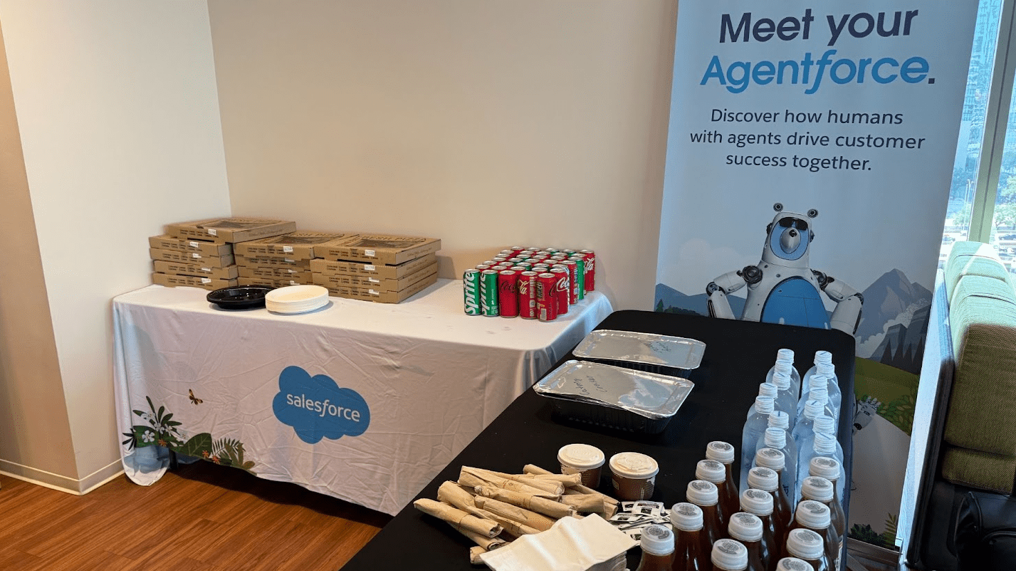 Lunch table: pizza and soda. Banner behind reads: Meet your Agentforce. Discover how humans with agents drive customer success together.
